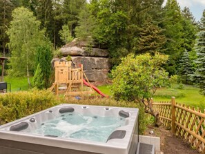 A hot tub surrounded by a wooden fence, a wooden play structure with a slide, and dense greenery. - Vacation home Dunja by Interhome (Oybin)