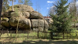 A large rock formation surrounded by trees and a wooden fence.