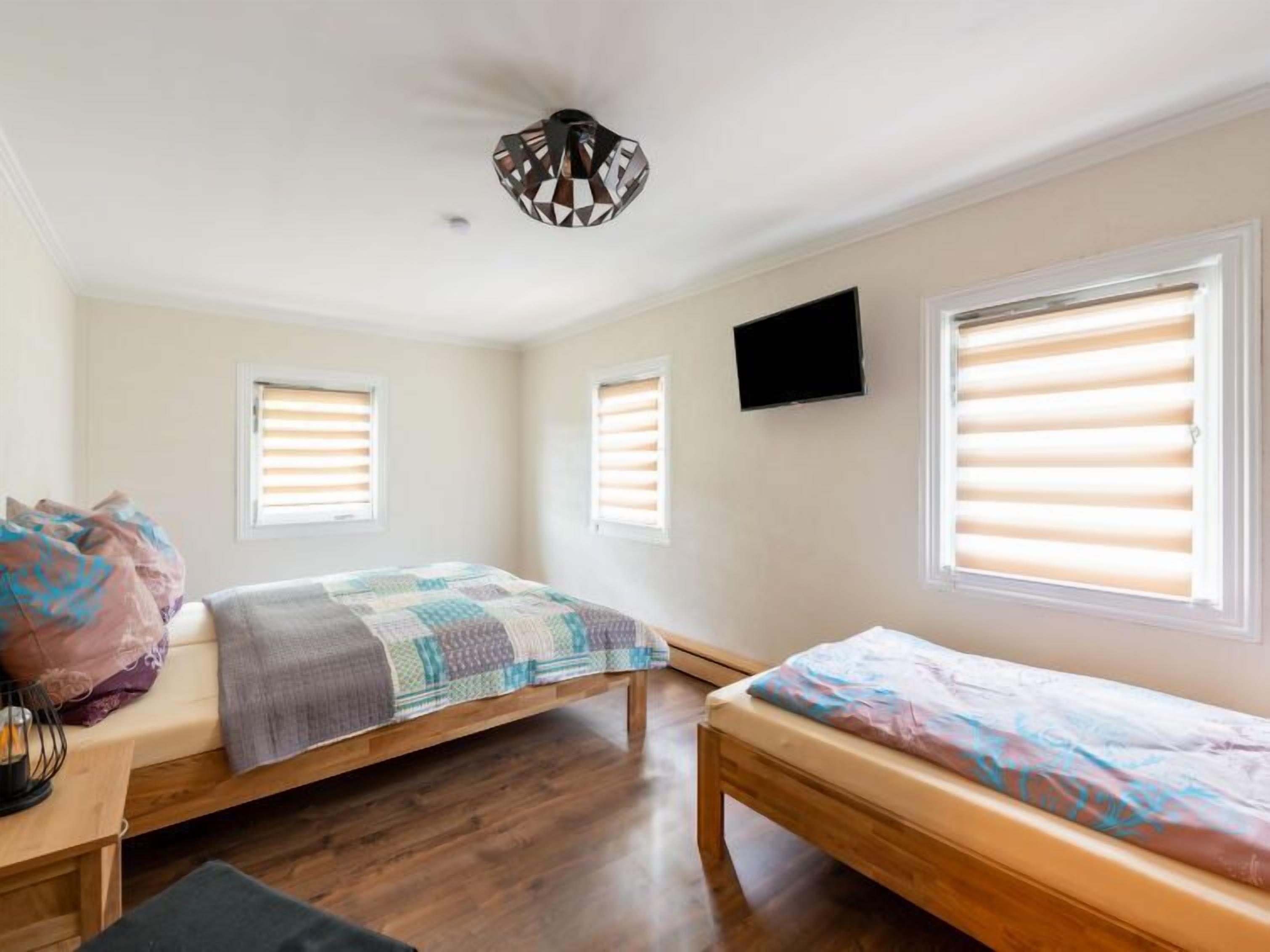 A bedroom with two beds, a TV, and two windows with blinds.