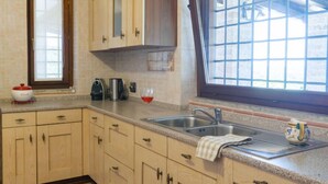 Une cuisine avec des meubles de couleur bois clair, un évier en acier inoxydable et une fenêtre à carreaux.