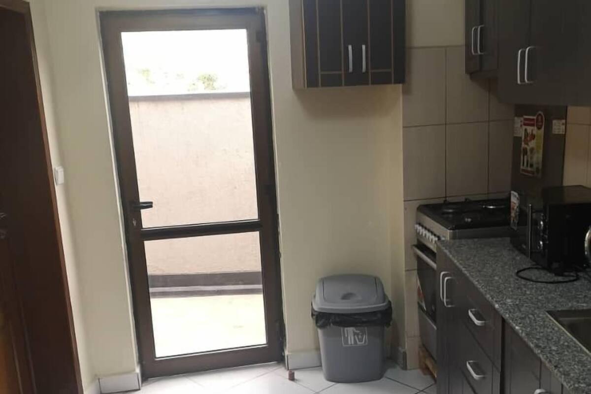 A kitchen with a tiled floor, dark cabinets, a stove, and a trash bin.
