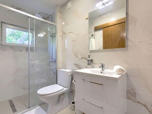 Ein modernes Badezimmer mit einer gläsernen Duschkabine, einer weißen Toilette und einem Waschtisch mit Spiegel.