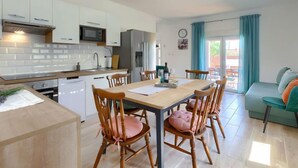 A modern kitchen with white cabinets, a microwave, and a refrigerator. There is a dining table with chairs and a sofa in the living area. - Maslina by Interhome (Pula/Duga uvala)