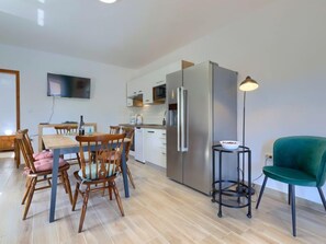 Una cocina moderna con un refrigerador grande, una mesa de comedor con sillas y una mesita auxiliar con un tazón.