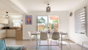 A modern kitchen with white cabinets and a wooden countertop, a dining area with a table and chairs, and a large window with a view of the outdoors. - Vacation home Vinci by Interhome (Royan)