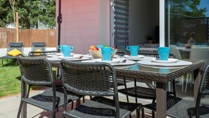 An outdoor patio with a table set for four, surrounded by wicker chairs, and a red umbrella providing shade. - Vacation home Vinci by Interhome (Royan)