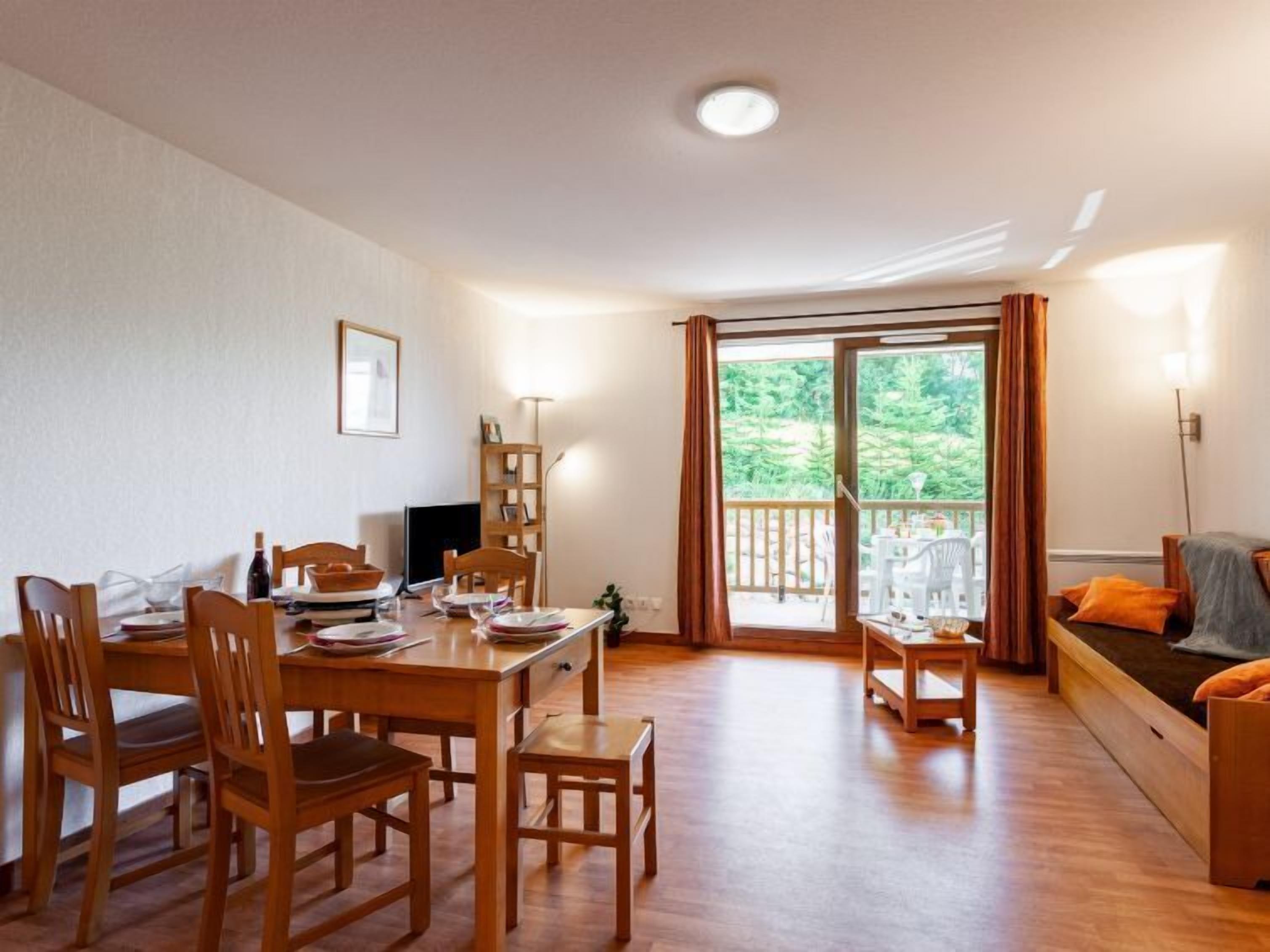 A dining area with wooden furniture, a television, and a view of greenery through a sliding door.