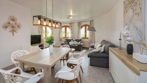 Un salon moderne avec une table à manger en bois, des chaises blanches, un canapé gris et un téléviseur.