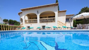 Une piscine ornée d’une mosaïque représentant un dauphin, un bâtiment blanc avec des arcades et des espaces de détente en plein air.