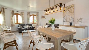 Un salon moderne avec un canapé gris, des chaises blanches, une table à manger en bois et un luminaire suspendu.