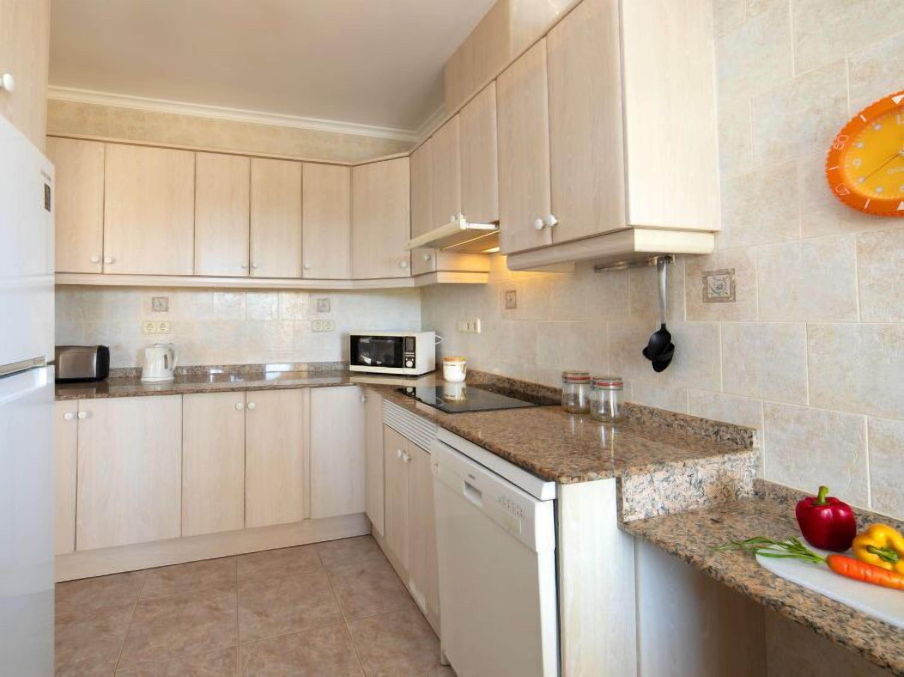 A kitchen with light-colored cabinets, a microwave, a toaster, and a dishwasher. There are jars on the counter and a red bell pepper and a yellow bell pepper on the counter.