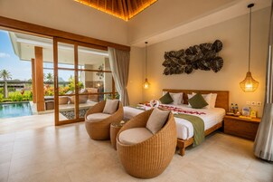 Habitación de hotel con una cama grande, dos sillas de mimbre, vista a una piscina y un jardín tropical.