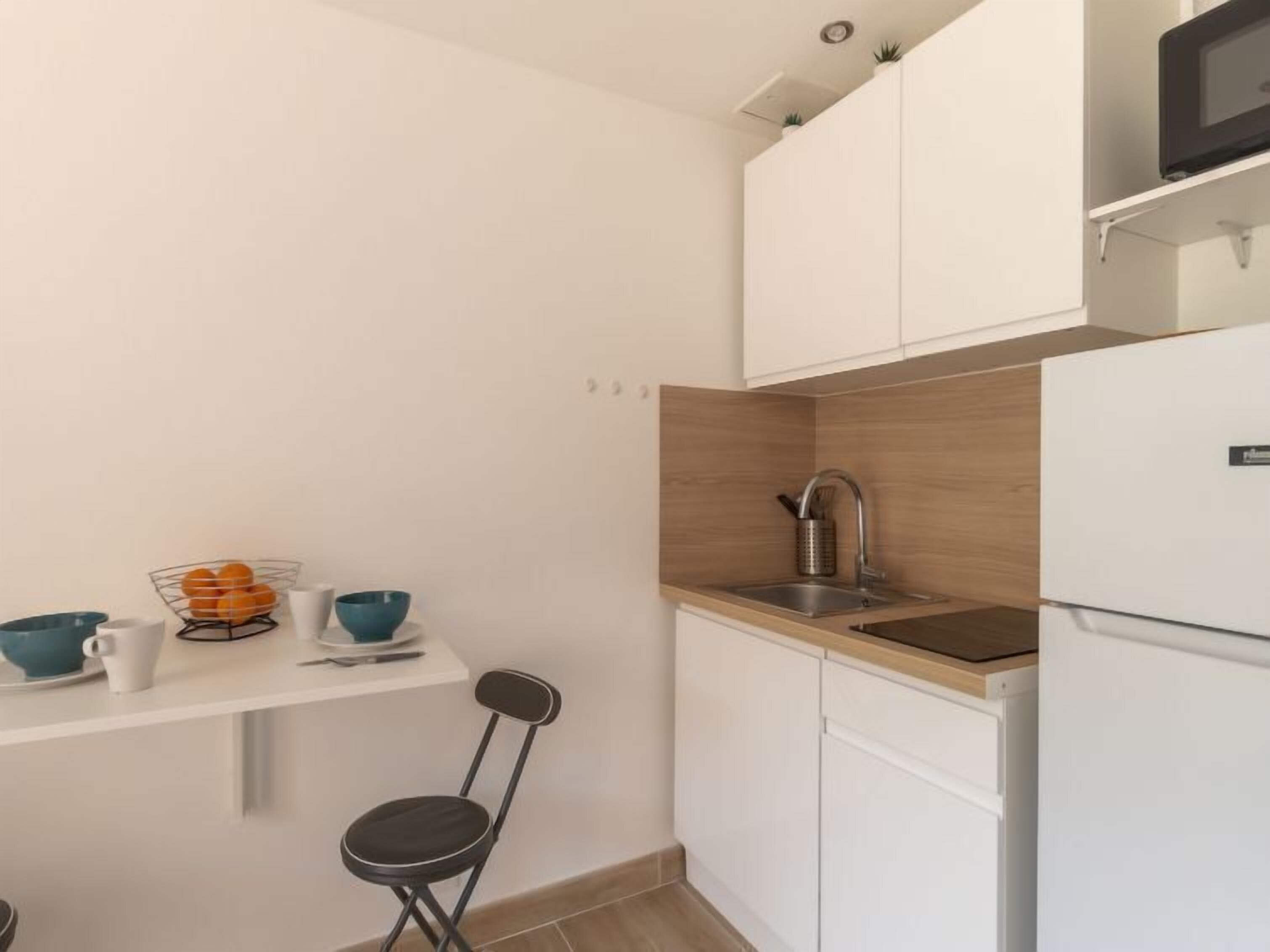 Eine kleine Küche mit weißen Schränken, einer Holz Arbeitsplatte, einer Spüle und einer Mikrowelle.