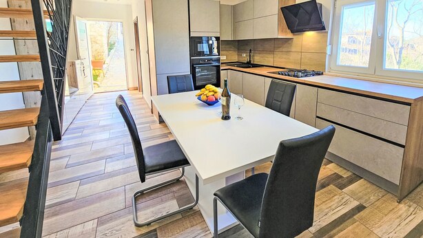 Een moderne keuken met een eethoek, houten vloer en een televisie boven de counter.