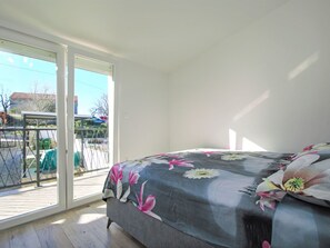 Ein Schlafzimmer mit Bett, einer Schiebetür zu einem Außenbereich und Blick ins Freie.