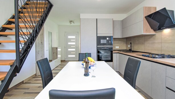 Una cocina moderna con comedor, escalera de madera y electrodomésticos integrados.