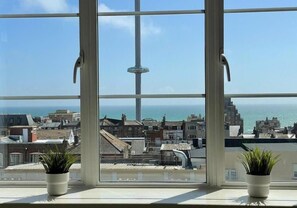 A window with a view of a cityscape and the sea, featuring a tall tower and two potted plants on the windowsill. - Southern View 2 By My Getaways (Brighton)