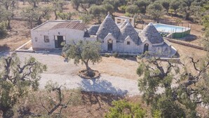 A traditional stone building with a flat-roofed main structure and conical-roofed extensions, surrounded by olive trees and a pool. - TD Trulli Albapetra Pool Olive Trees (Polignano a Mare)