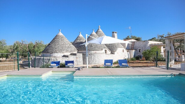 A swimming pool with lounge chairs and stone buildings with conical roofs. - TD Trulli Albapetra Pool Olive Trees (Polignano a Mare)