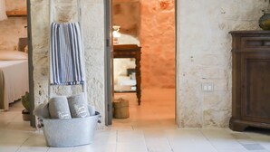 A room with a metal bucket containing rolled towels, a striped towel hanging on a wall, and a wooden cabinet. - TD Trulli Albapetra Pool Olive Trees (Polignano a Mare)