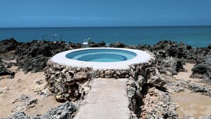 A circular pool with a clear blue center, surrounded by rocky terrain and a view of the ocean. - Casa Los Sue os in Punta Cana (Sosúa)
