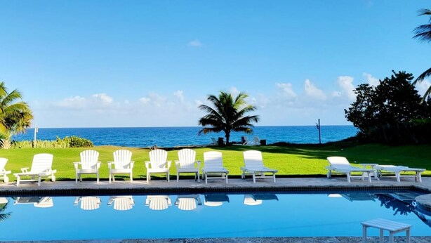 A pool with white chairs and a view of the ocean. - Casa Los Sue os in Punta Cana (Sosúa)