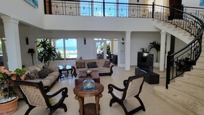 A spacious living room with a high ceiling, a staircase, and large windows offering a view of the outdoors. - Casa Los Sue os in Punta Cana (Sosúa)