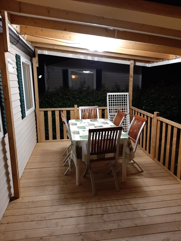 An outdoor wooden deck with a table and chairs, surrounded by a wooden railing.