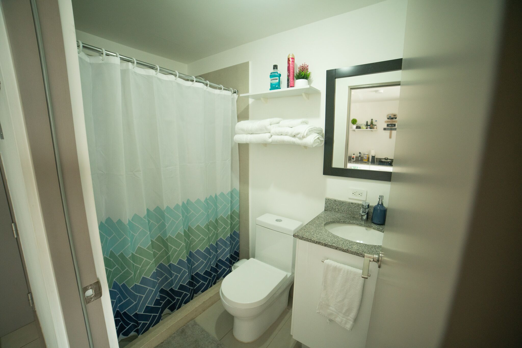 A bathroom with a shower curtain, toilet, sink, and a mirror.