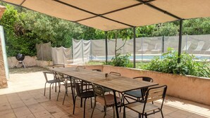 Un porche techado con una mesa y sillas de madera, una parrilla y vistas a una piscina.