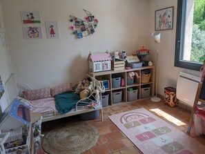 Ein gemütliches Kinderzimmer mit Bett, Aufbewahrungsboxen, einem Spielhaus und einem Teppich.
