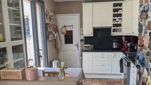 Una cocina con armarios blancos, encimera negra y piso de baldosas. Cuenta con una mesa de comedor con sillas, un colgador para ollas y una pizarra con un mensaje de bienvenida.