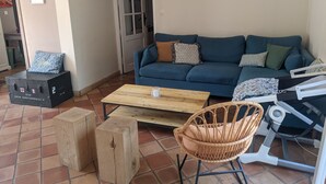 Una sala de estar con un sofá azul, una mesa de centro de madera, una silla de mimbre y una mesita con un cochecito de bebé.