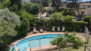 Una piscina rodeada de vegetación, con sillas de descanso y una valla.