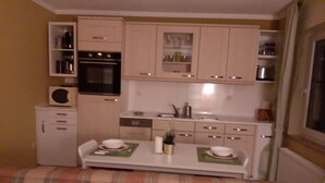 Una cocina compacta con armarios blancos, horno empotrado y comedor con mesa para dos.