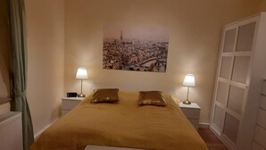 Un dormitorio con una cama, dos lámparas de noche, una mesita de noche, una ventana con cortinas y un cuadro colgado en la pared.