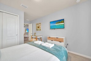 Un dormitorio con cama, escritorio, silla, televisión y un cuadro en la pared.