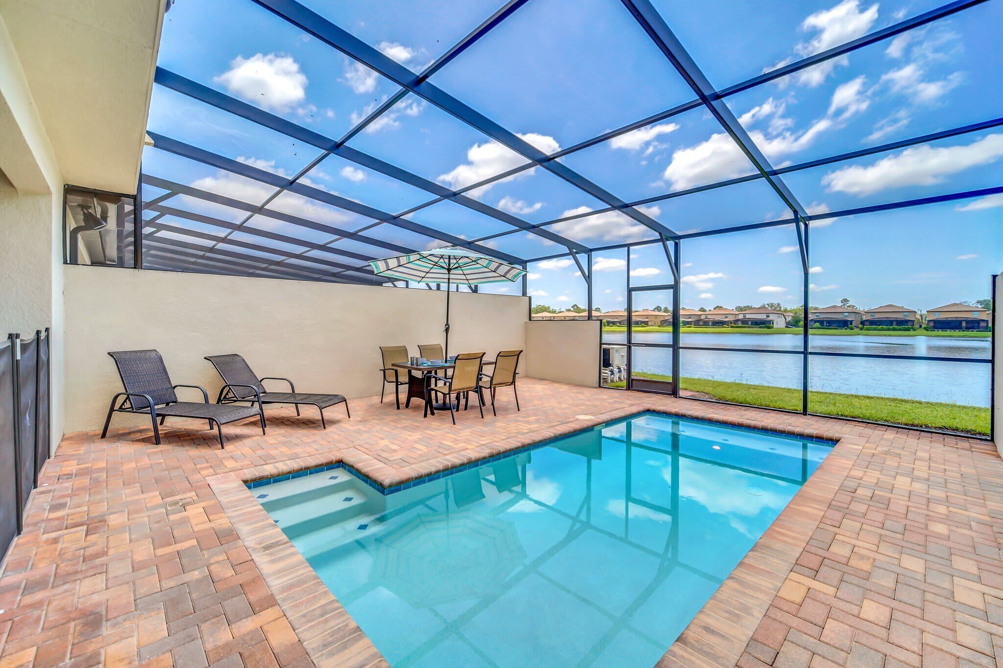 An indoor swimming pool with a patio area, a table with chairs, and a view of a lake.