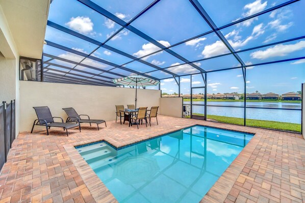 An indoor swimming pool with a patio area, a table with chairs, and a view of a lake. - Stunning Lake View! Themed Bedrooms With Comfortable and Sophisticated Decor (Kissimmee)