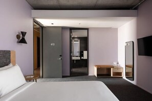 A modern hotel room with a bed, a desk, a mirror, and a door leading to a bathroom. - Alex Hotel (Northbridge)