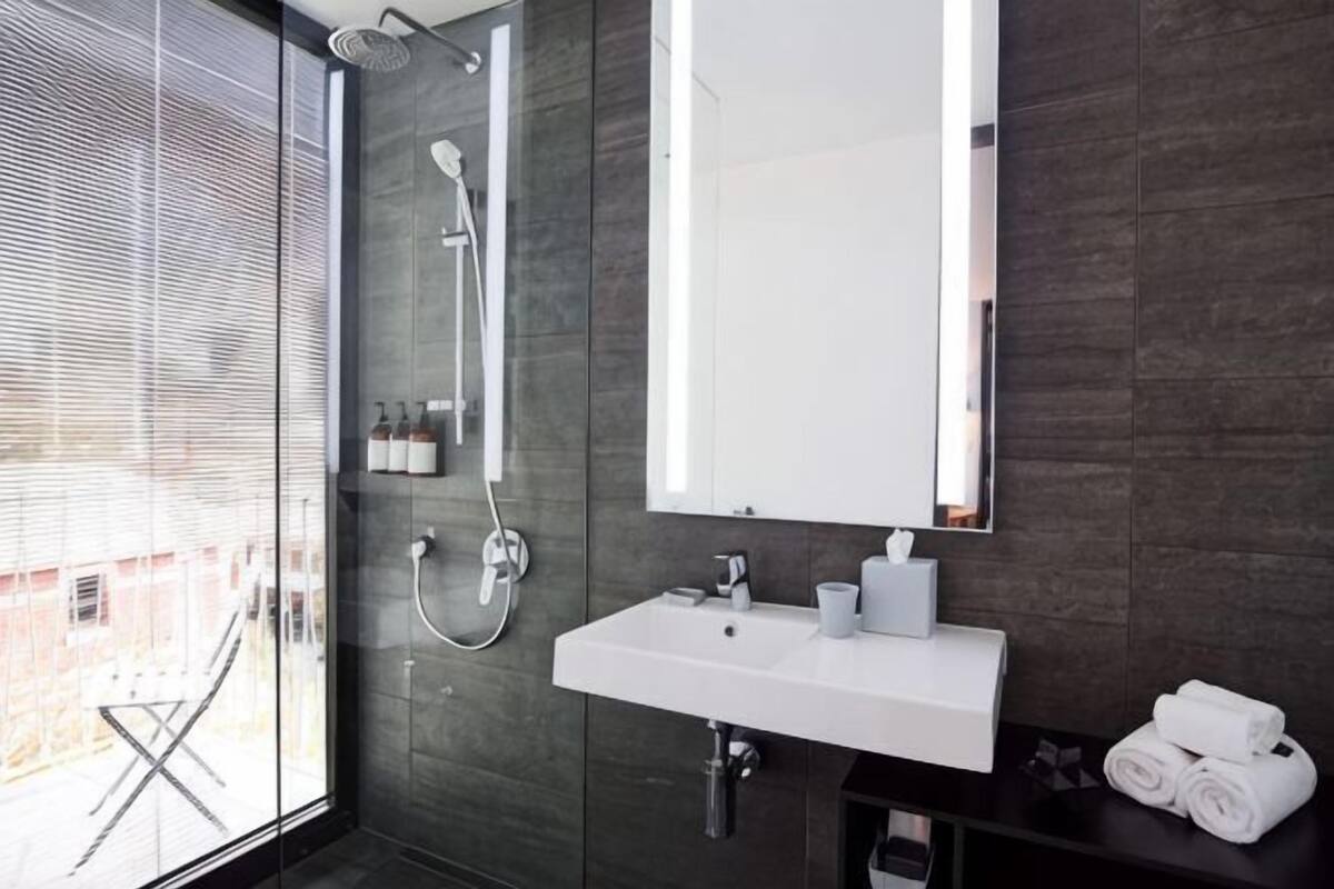 Un baño moderno con ducha de vidrio, lavamanos blanco y espejo grande.