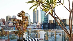 A rooftop terrace with a city view, seating area, and a potted plant. - Alex Hotel (Northbridge)
