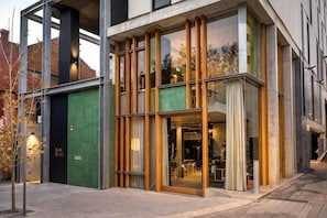 A modern building with large glass windows, a green door, and a visible interior with tables and chairs. - Alex Hotel (Northbridge)