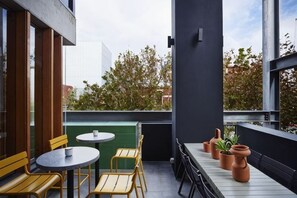 A balcony with wooden chairs and tables, potted plants, and a view of trees and buildings. - Alex Hotel (Northbridge)