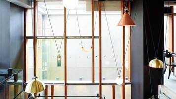 Un interior moderno con vigas estructurales a la vista, barandilla de vidrio e iluminación colgante.