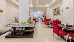 Une salle à manger d’hôtel avec un buffet, des chaises à revêtement rouge et un lustre.