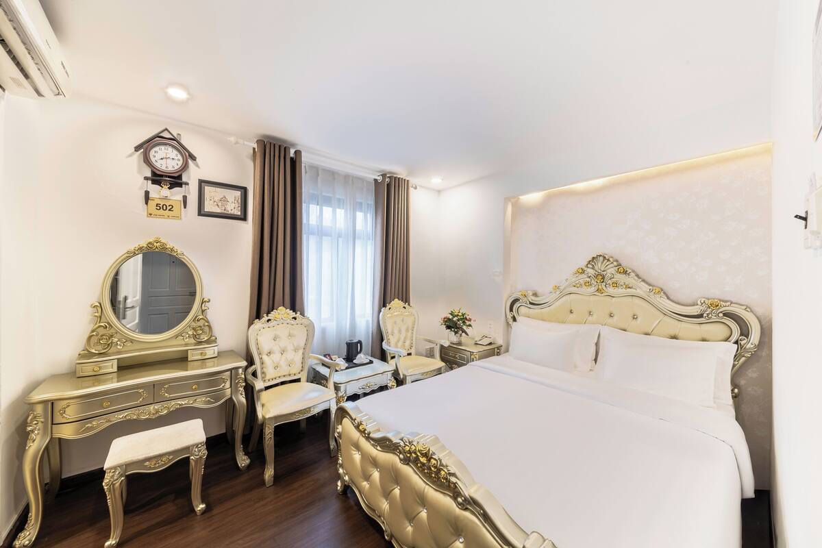 A luxurious bedroom with a large bed, a vanity with a mirror, and two chairs.