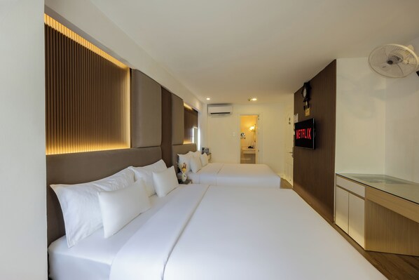 Habitación de hotel con dos camas, televisión, aire acondicionado y ventilador.