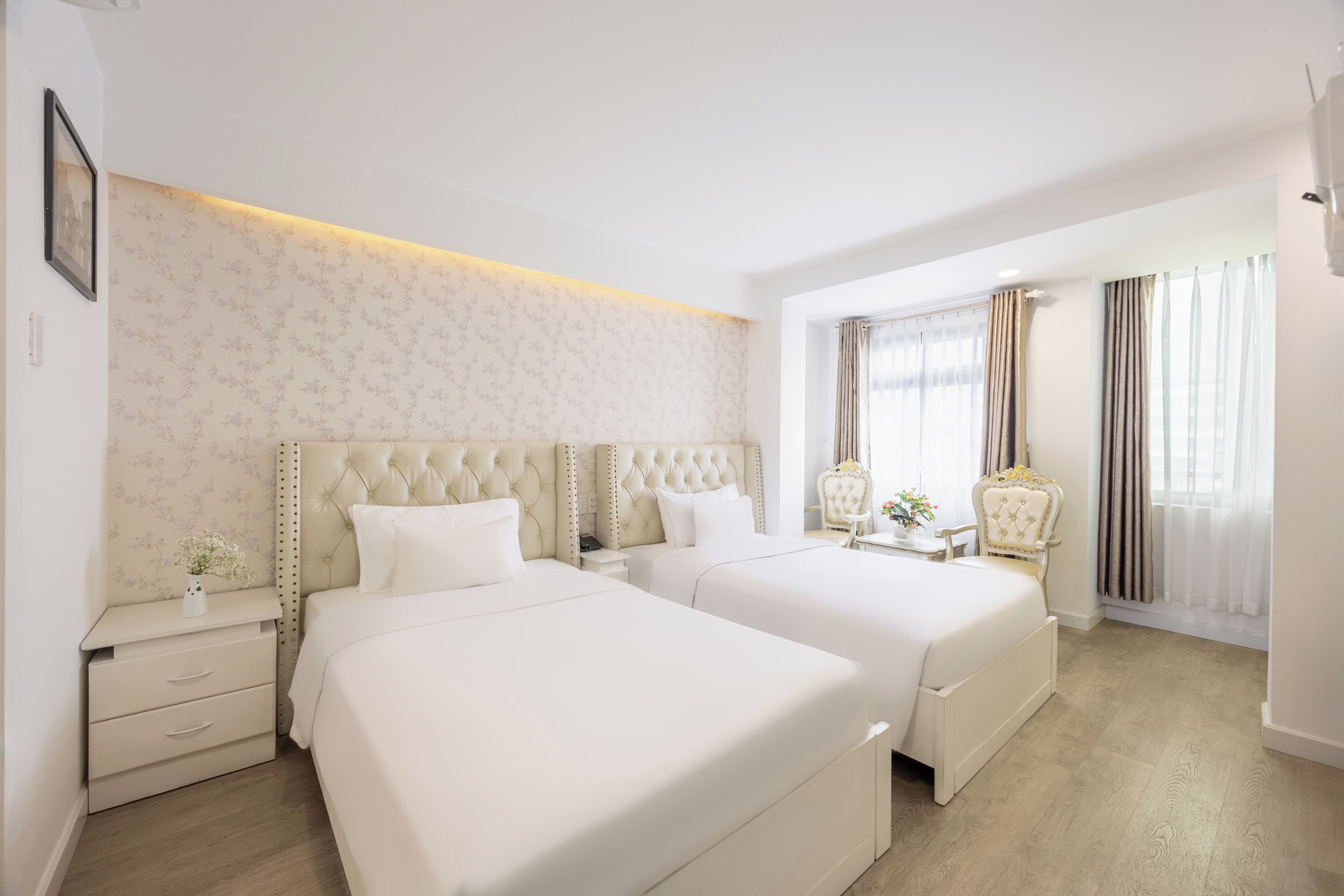 Ein Hotelzimmer mit zwei Betten, einem Nachttisch, einem Stuhl und einem Fenster mit Vorhängen.