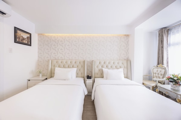 A hotel room with two beds, a nightstand with a phone, a chair, and a table with a vase of flowers.